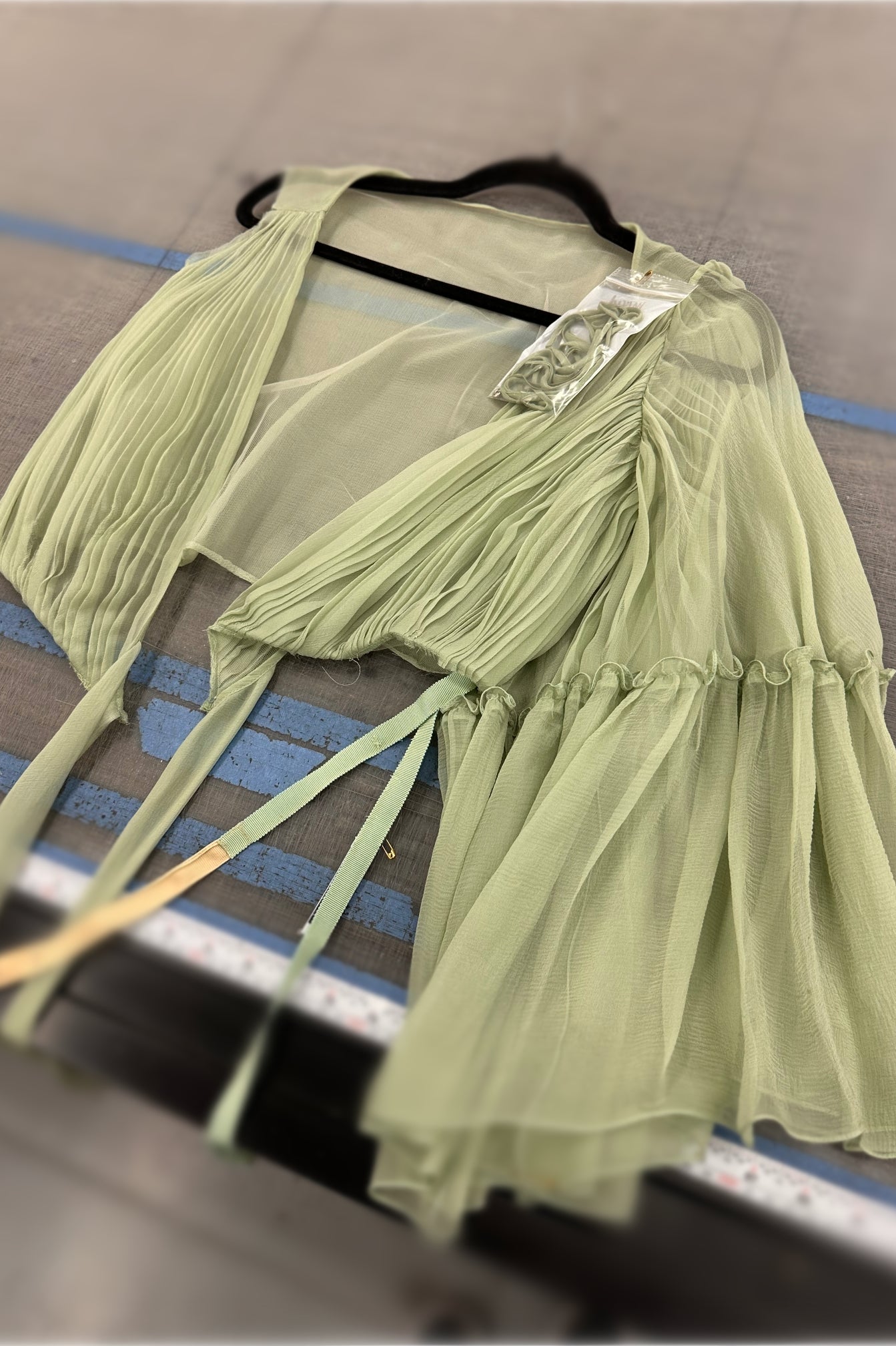 Light green silk chiffon bodice on a hanger with a visible tag against a background