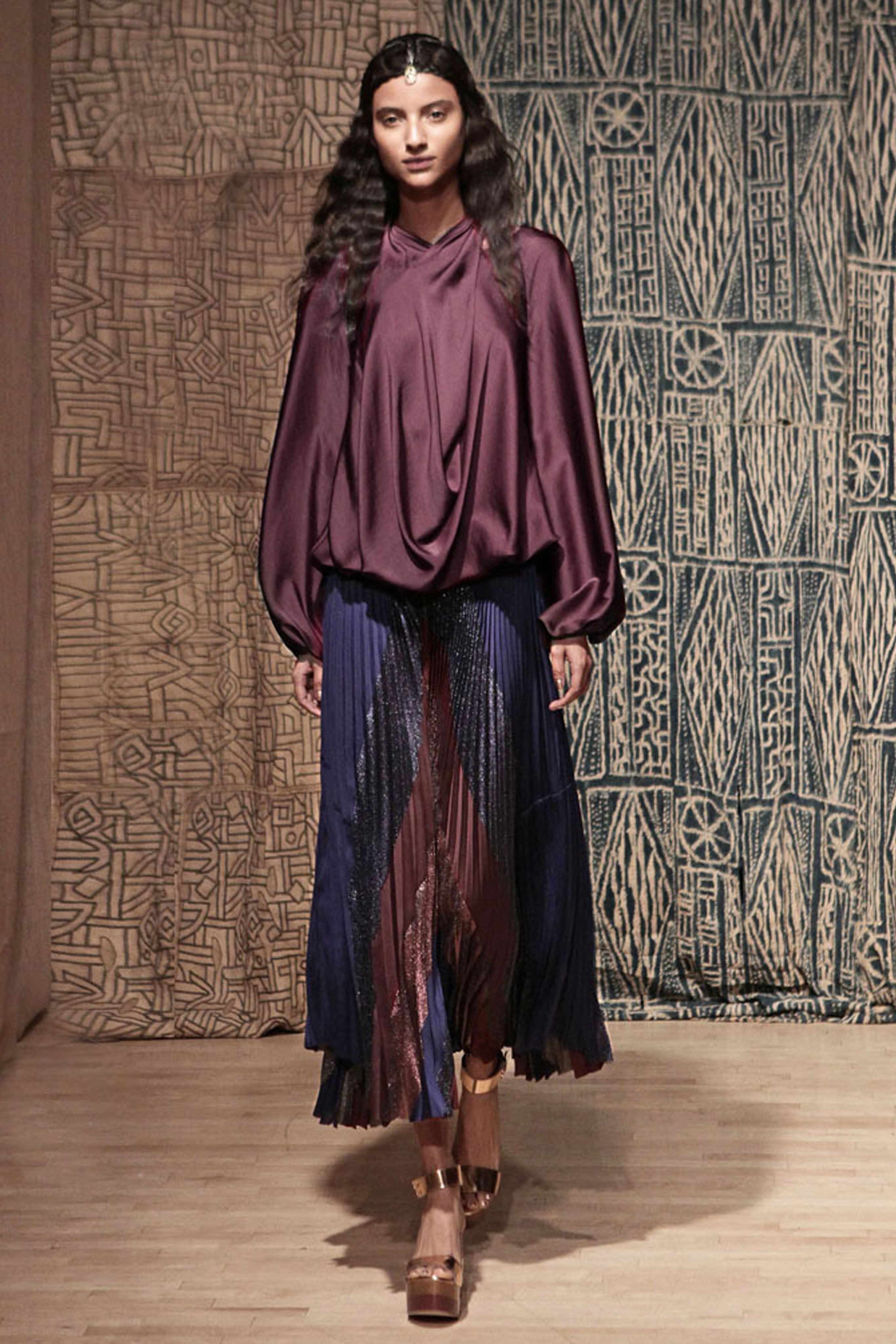 Model wearing a plum colored top with a sunburst accordion skirt that is different fabrics 