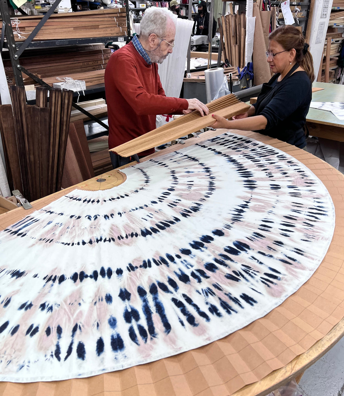 Pleating specialists aligning a printed circular fabric panel on a large pleating table